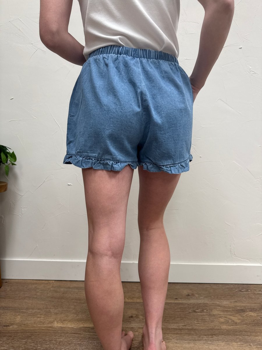 Back view of denim ruffle hem shorts on model showing rear pockets and fit — Three:Twelve Boutique