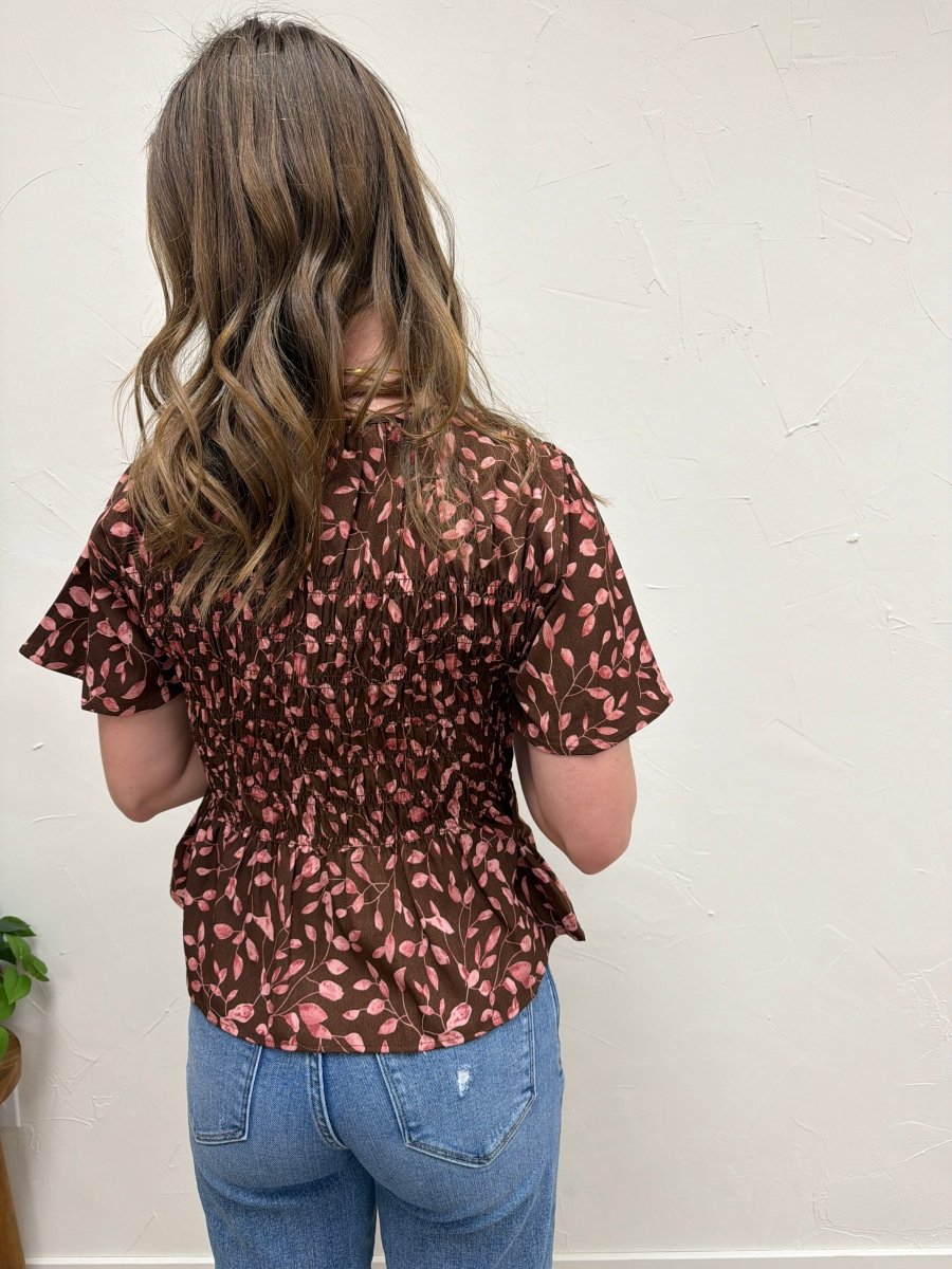 Back view of floral peplum blouse on model highlighting smocked detail — Three:Twelve Boutique